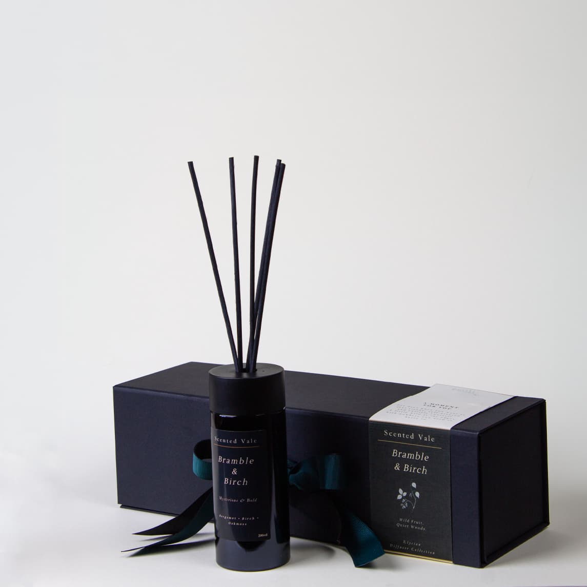 A reed diffuser bottle with black reeds stands in front of its matching dark box. The label reads 'Scented Vale Bramble & Birch'