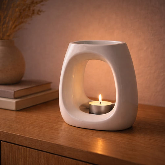 Cove White ceramic wax warmer with a lit candle on a wooden surface during the evening