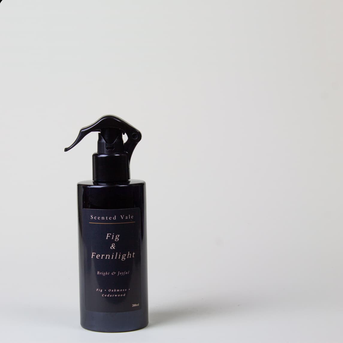 A dark violet blue spray bottle with a black sprayer, labeled 'Scented Vale Fig & Fernlight', set against a plain light grey background.