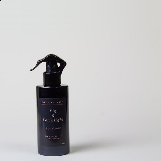 A dark violet blue spray bottle with a black sprayer, labeled 'Scented Vale Fig & Fernlight', set against a plain light grey background.