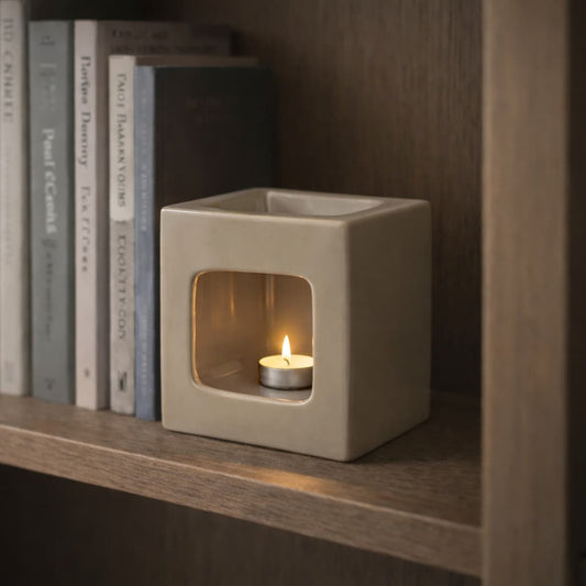 The Frame Ceramic Wax Warmer in Soft sand, shown on a bookshelf during the day