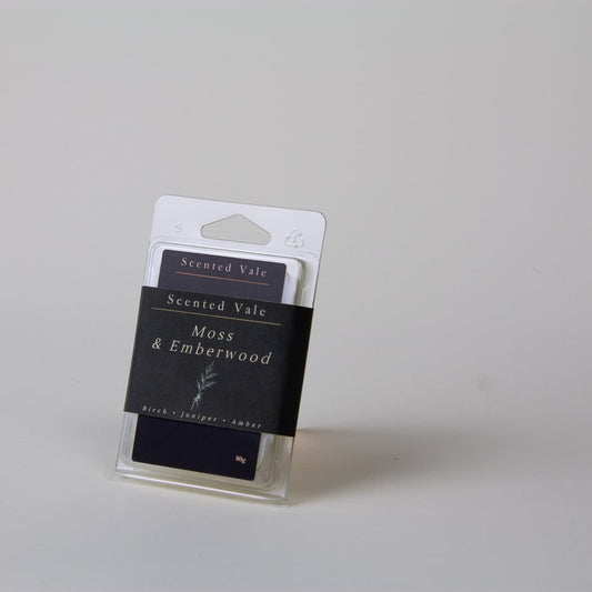 A packaged wax melt standing upright on a plain light grey background. The clear plastic package contains a dark label reading 'Scented Vale Moss & Emberwood' and smaller text 'Bark - Juniper - Amber'.