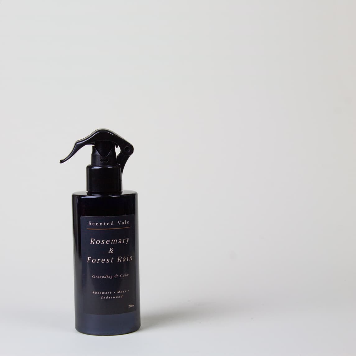 A dark navy blue spray bottle with a black trigger sprayer, labeled 'Scented Vale Rosemary & Forest Rain', set against a plain light grey background.