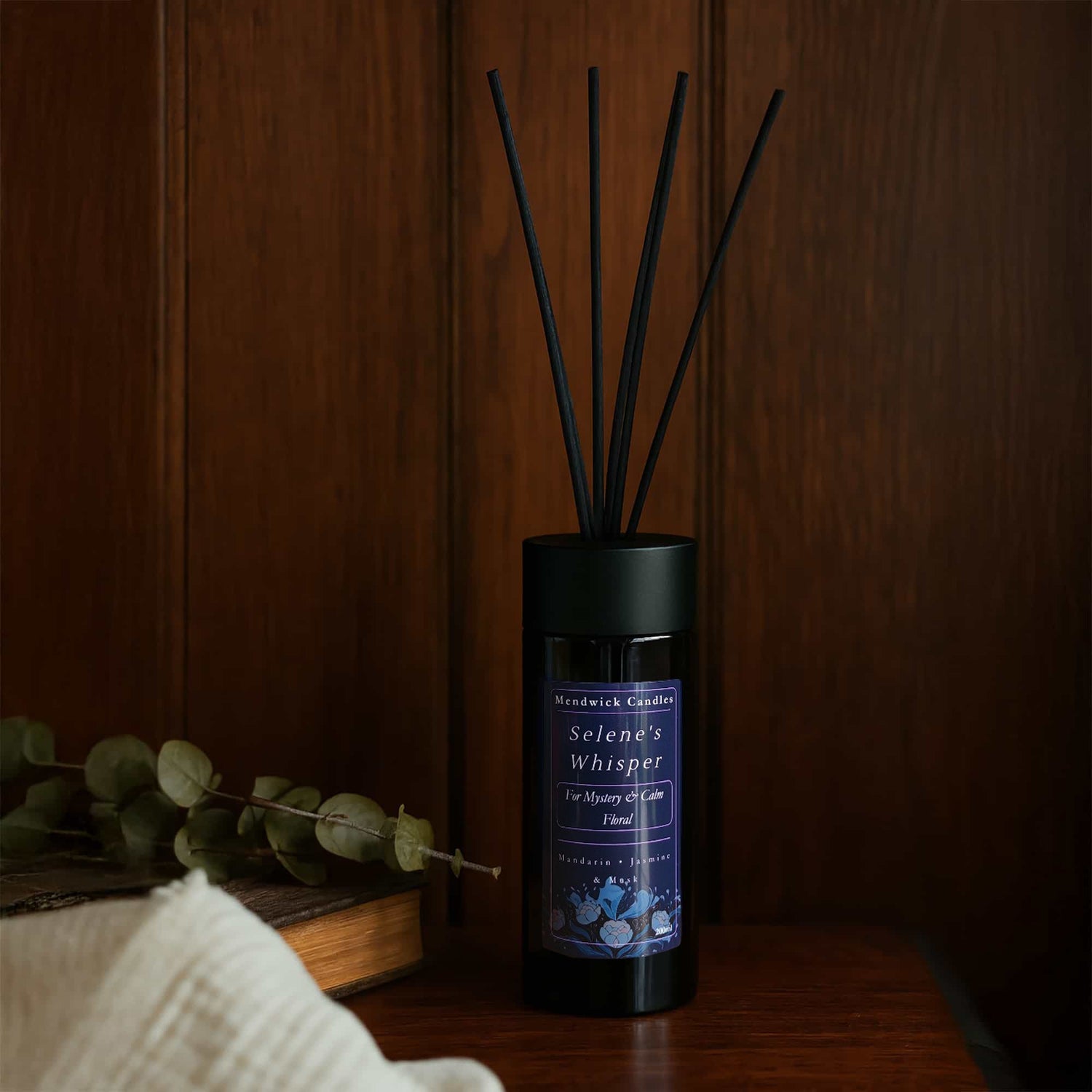 Reed Diffuser on a dark wooden table with soft fabric, book and eucalyptus