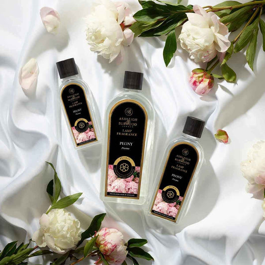 Three bottles of Ashleigh & Burwood Peony Lamp Fragrance on a white cloth with peonys scattered around