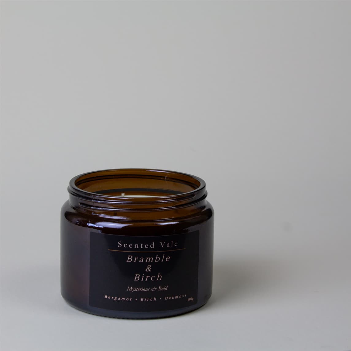 An amber glass jar candle with a black label reading 'Scented Vale Bramble & Birch' on a neutral light grey background.