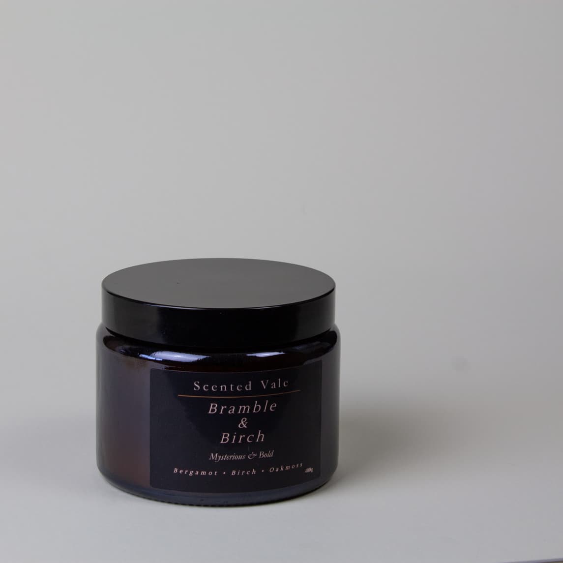 A dark amber glass jar candle with a black lid and a black label reading 'Scented Vale Bramble & Birch' on a light grey background.