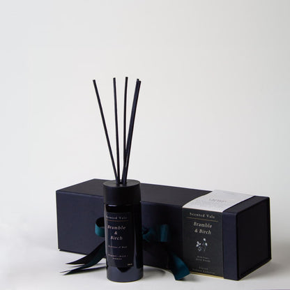 A reed diffuser bottle with black reeds stands in front of its matching dark box. The label reads 'Scented Vale Bramble & Birch'