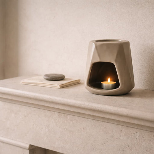 The Cairn Ceramic Wax warmer with a lit candle on a stone fireplace