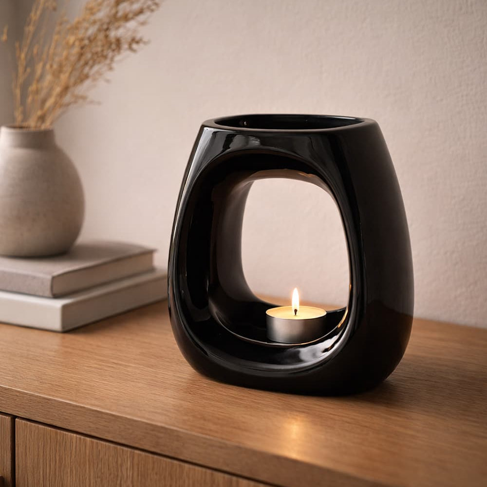 Cove Black ceramic wax warmer with a lit candle on a wooden surface