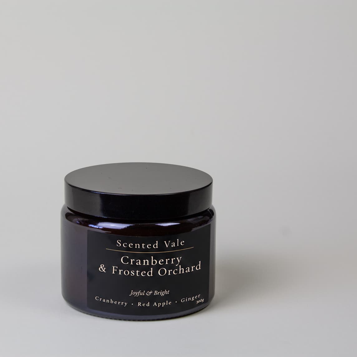 A dark glass jar candle with a black lid and a black label reading 'Scented Vale Cranberry & Frosted Orchard' on a light gray background.