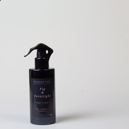 A dark violet blue spray bottle with a black sprayer, labeled 'Scented Vale Fig & Fernlight', set against a plain light grey background.