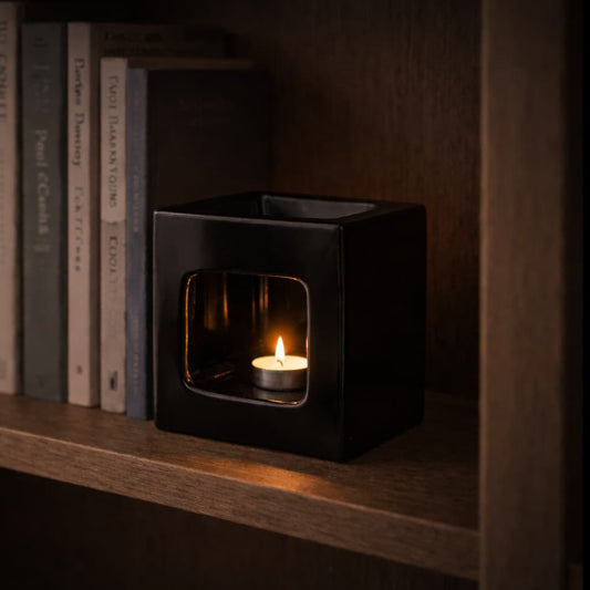 The Frame Ceramic Wax Warmer in black, shown on a bookshelf during the evening
