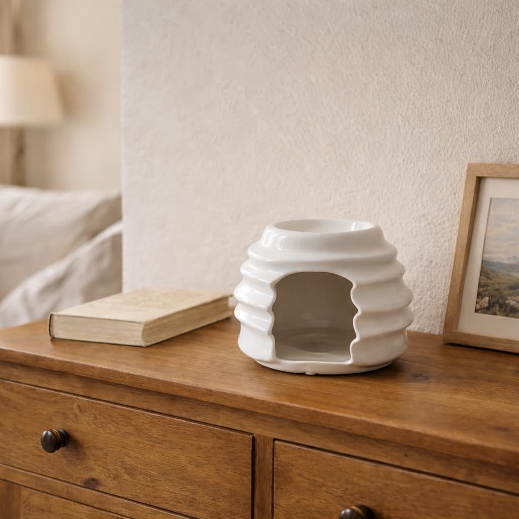 White ceramic Hive Wax Warmer on a wooden dresser with a book and framed picture in the background.